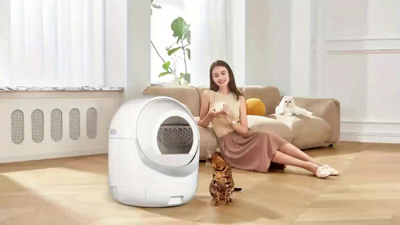 Woman sitting on a couch with a cat next to a self-cleaning litter box in a modern living room.