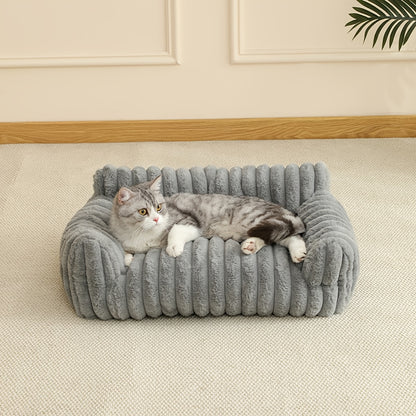 Gray cat lying on a plush cat sofa in a room with beige walls and a wooden baseboard.