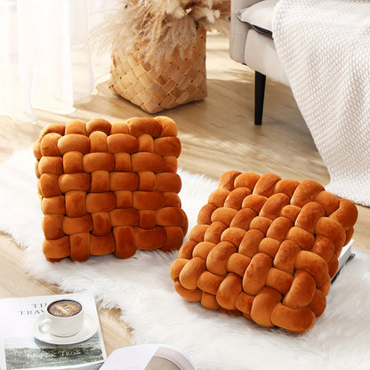 Two orange woven square cushions on a white surface with a blurred background