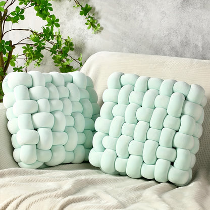Two light blue woven pillows on a beige sofa with a neutral background